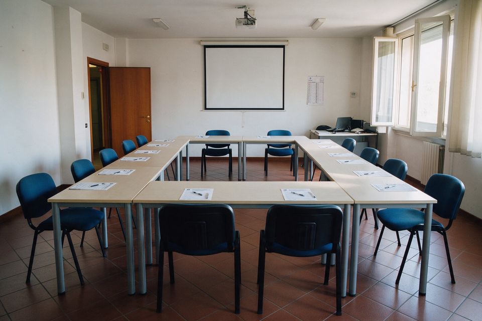 Aula con i tavoli a ferro di cavallo, le sedie blu e lo schermo per le proiezioni